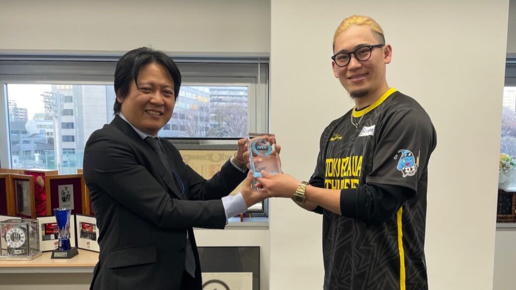 ＦＰパートナー徳山様からトロフィーを受け取る宮食行次選手。徳山様は上下黒いスーツ。宮式選手は所沢サンダースのユニフォームを着用してしている。